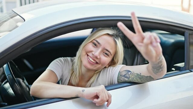 Young beautiful hispanic woman sitting on car doing victory gesture at street