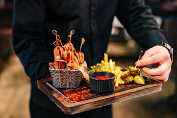 Waiter hold plate with corn dog, french fries and sauce in pub