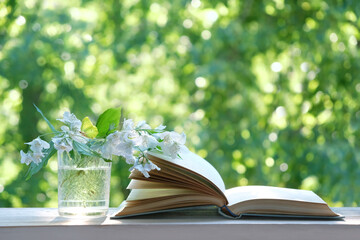 Jasmine flowers in vase and open book on table close up, abstract green natural background. symbol...