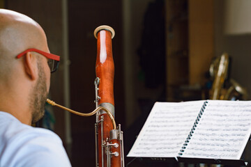 rear view of man reading sheet music and playing bassoon at home, focus on bassoon