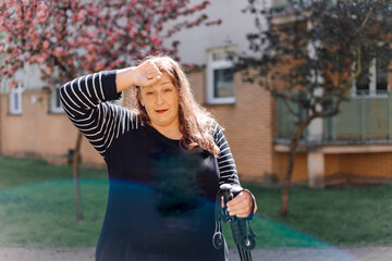 Overweight woman is very tired after training in Nordic walking with sticks , she is standing...