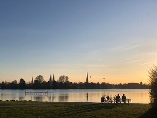Two people sit on a bench at sunset near the lake in Lubeck, Germany