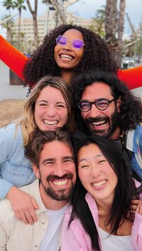 Vertical portrait of a group of friends laughing together and looking at camera. Five young multiracial people smiling and having fun. Joyful startup team coworkers celebrating and bonding together