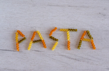 The word pasta is laid out of fusilli pasta on a white wooden background
