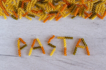 The word pasta is laid out of fusilli pasta on a white wooden background