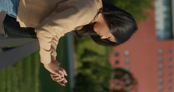 Young teenage Latina college student using social networks with her smartphone in a park, vertical shot
