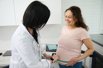 Female doctor obstetrician gynecologist measures the height of the fundus of the uterus, the volume...