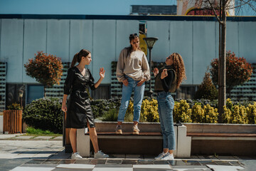 Lovely girl in black overcoat explaining something to her curly haired friend. Their long haired brunette friend is standing on a bench and listening to the conversation