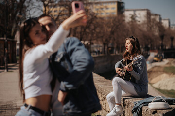 Fototapeta na wymiar Lovely brunette girl playing guitar while a couple is taking a selfie