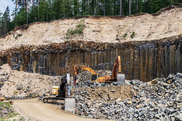 Basalt mining. Yellow excavators in a basalt quarry near the forest.