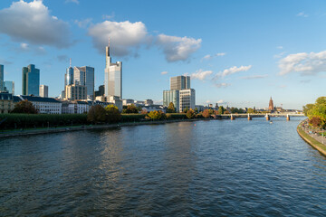 Stunning  of Frankfurt's skyline, featuring its iconic skyscrapers, traffic on the bridge, and a bustling promenade on a partly cloudy day.