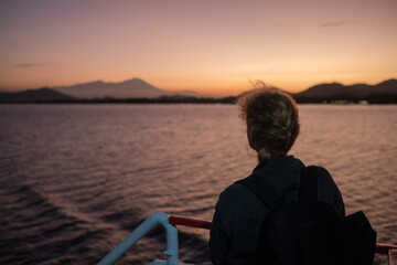 Fototapeta premium Young Blonde Woman with a Backpack Traveling on a Ferry, Admiring a Stunning Ocean Sunrise