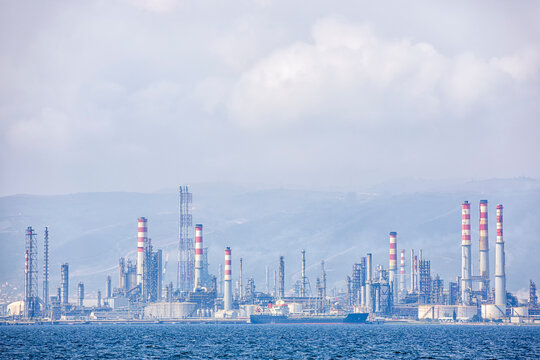 View of oil refinery near to sea. An oil refinery or petroleum refinery is an industrial process plant where petroleum (crude oil) is transformed and refined into useful products such as gasoline.