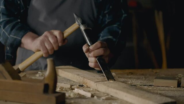 Sawmill, Middle-aged builder Works with a chisel knocking chips out of wood Working with tools In a carpenter's workshop Concentrated on the task making parts In craftsman's workshop, carpentry tools
