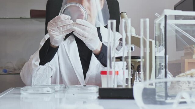 Slow motion. The camera moves from bottom to top. Adult young female researcher in a white coat and protective mask in the process of working with insects in the laboratory