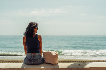 beautiful brunette girl looks at the sea sitting opposite
