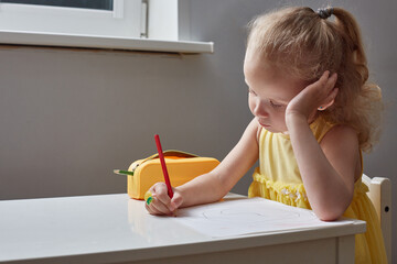 A bored girl draws with pencils at table at home.