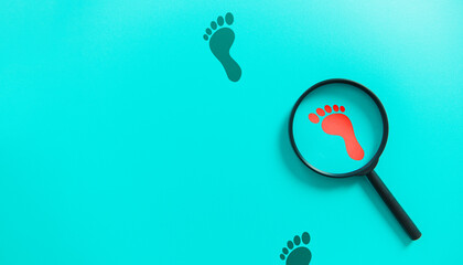 Magnifying glass magnifying red bare footprints on blue background. Investigation and detective...