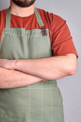 A man in a kitchen apron. Chef work in the cuisine. Cook in uniform, protection apparel. Job in food service. Professional culinary. Green fabric apron, casual stylish clothing. Handsome baker posing