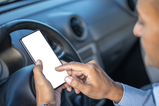 Detail of the hand of a driver holding a mobile phone with a blank screen on the steering wheel of the car with copy space.
