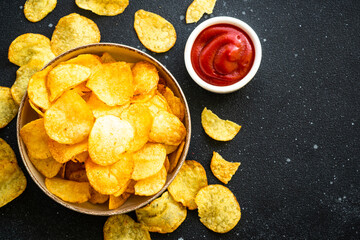 Potato chips and ketchup sauce on black table. Top view with copy space.