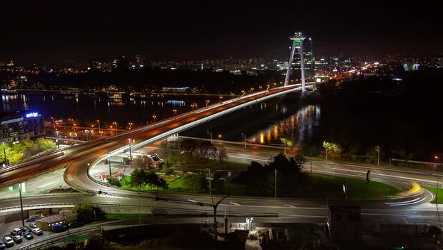 A stunning timelapse of Bratislava's skyline at night, featuring an aerial view of the illuminated bridge, busy traffic, and vibrant city lights reflecting on the Danube River during autumn season.