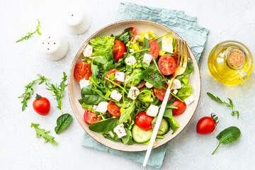 Green salad with spinach, arugula and tomatoes with olive oil. Top view on white.