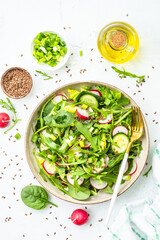 Green salad with spinach, arugula and radish with olive oil on white table. Top view with copy space.