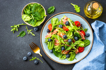 Green salad with fresh prosciutto, green leaves mix and tomatoes at dark table. Top view with copy space.