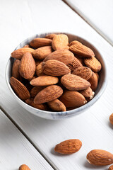 Fresh almonds in a bowl on white wooden background. Bowl of almonds on wooden background. Close-up. 