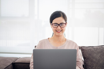 asian mature woman working on laptop in living room at home office. asian professor  using computer remote teaching , virtual training, e-learning, watching online education webinar at home