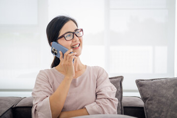 Happy stylish mature woman remote working from home distance office on laptop talking on phone . Smiling middle aged business lady using computer watching webinar sit on couch in living room.