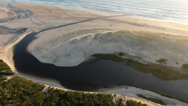 Drone view of the mouth of the Huchet Current at sunset, when the ocean forms a river behind the dune in Moliets, France