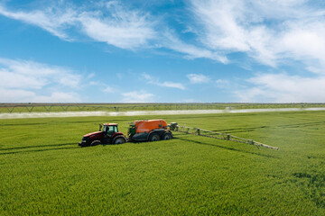 Aerial view of tractor spray fertilizer on green field. Farming tractor plowing and spraying on field.