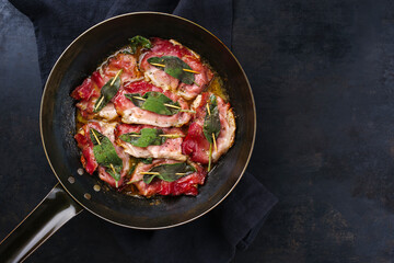 Traditional Italian fried pork saltimbocca alla Romana with Parma ham and sage leaves served as top view in a classic frying pan with copy space right