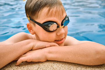 Smiling boy portrait in swimming goggles, Child swim in the pool, sunbathes, swimming in hot summer day. Relax, Travel, Holidays, Freedom concept.