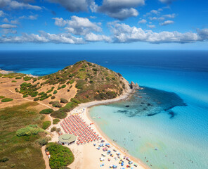 Fototapeta na wymiar Aerial view of colorful umbrellas, white sandy beach, people, blue sea, mountain with green forest, sky with clouds at summer sunny day. Tropical landscape. Travel in Sardinia, Italy. Top drone view