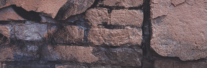 Old brick wall with peeling stucco. Weathered rough wall surface with brickwork. The wall is painted in different colors. Wide panoramic texture for background and design.