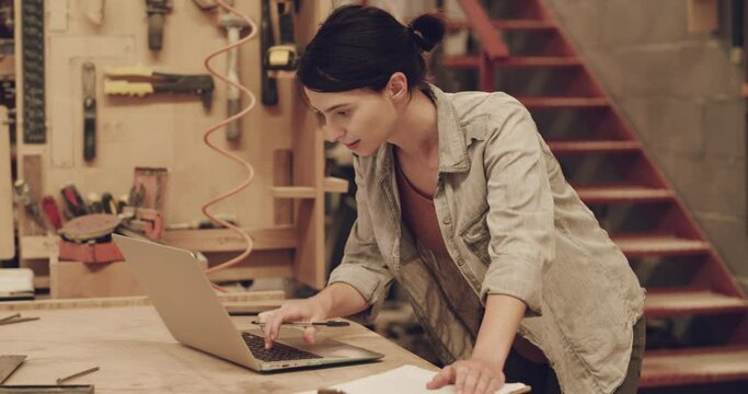 Woman, laptop and writing notes for carpentry in a workshop for small business. Female carpenter with technology for planning, online website and planning ideas for creative furniture project