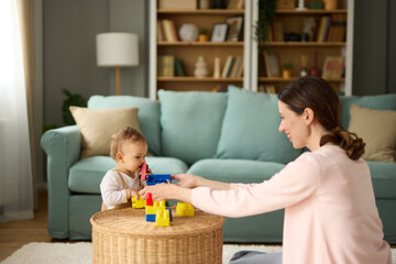 Mother and her baby boy playing with colored toy blocks at home