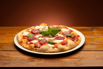 pizza with salami and tomatoes and mozzarella on the wooden table - 604399452