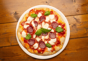 pizza with salami and tomatoes and mozzarella on the wooden table - 604399619