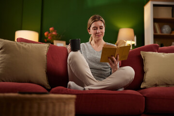 Obraz premium Mid adult woman enjoys reading a book on sofa at home