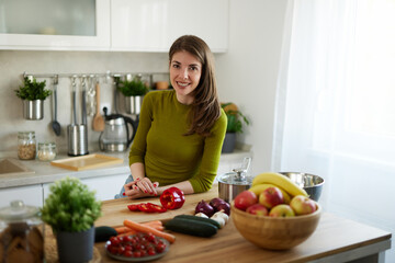Woman chopping red bell pepper on the wooden board in the kitchen