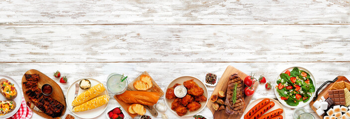 Summer BBQ food bottom border over a white wood banner background. Assortment of grilled meats, potatoes, vegetable dishes and smores platter. Top view with copy space.