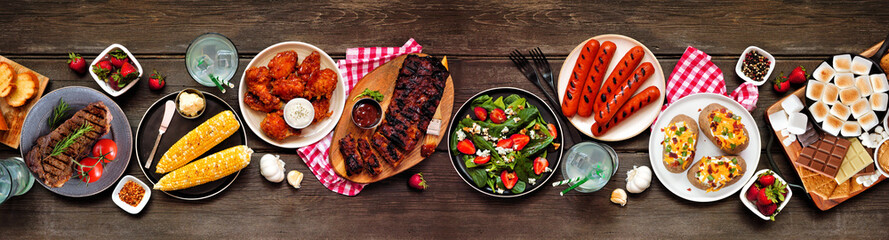 Summer BBQ food table scene over a dark wood banner background. Collection of grilled meats,...