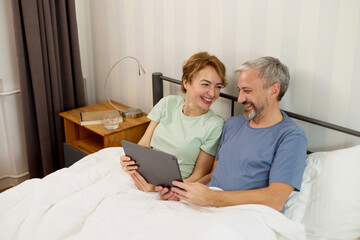 Obraz premium Smiling mature couple using digital tablet at home in bed