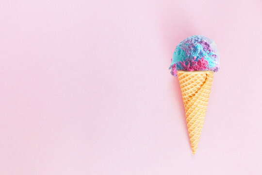 Single ice cream cone with pastel cotton candy ice cream over a textured pink background. Top view with copy space.