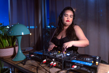 Fototapeta na wymiar fat Beautiful brazilian female DJ plays music at a party uses a counter-controller and a notebook in a night club