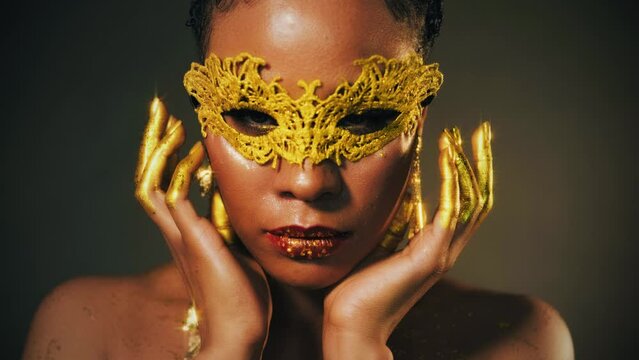 Portrait african woman face close up in golden carnival mask. Sexy girl fashion model perfect skin party evening holiday makeup glitter lip gloss hands lips in gold liquid paint. Fantasy lady queen 4k